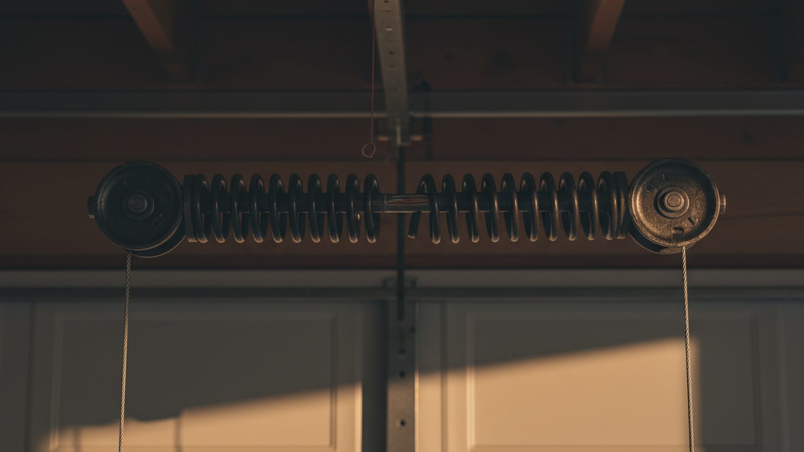 Close-up of a broken torsion spring mounted above a garage door with a visible gap in the coil where the spring snapped