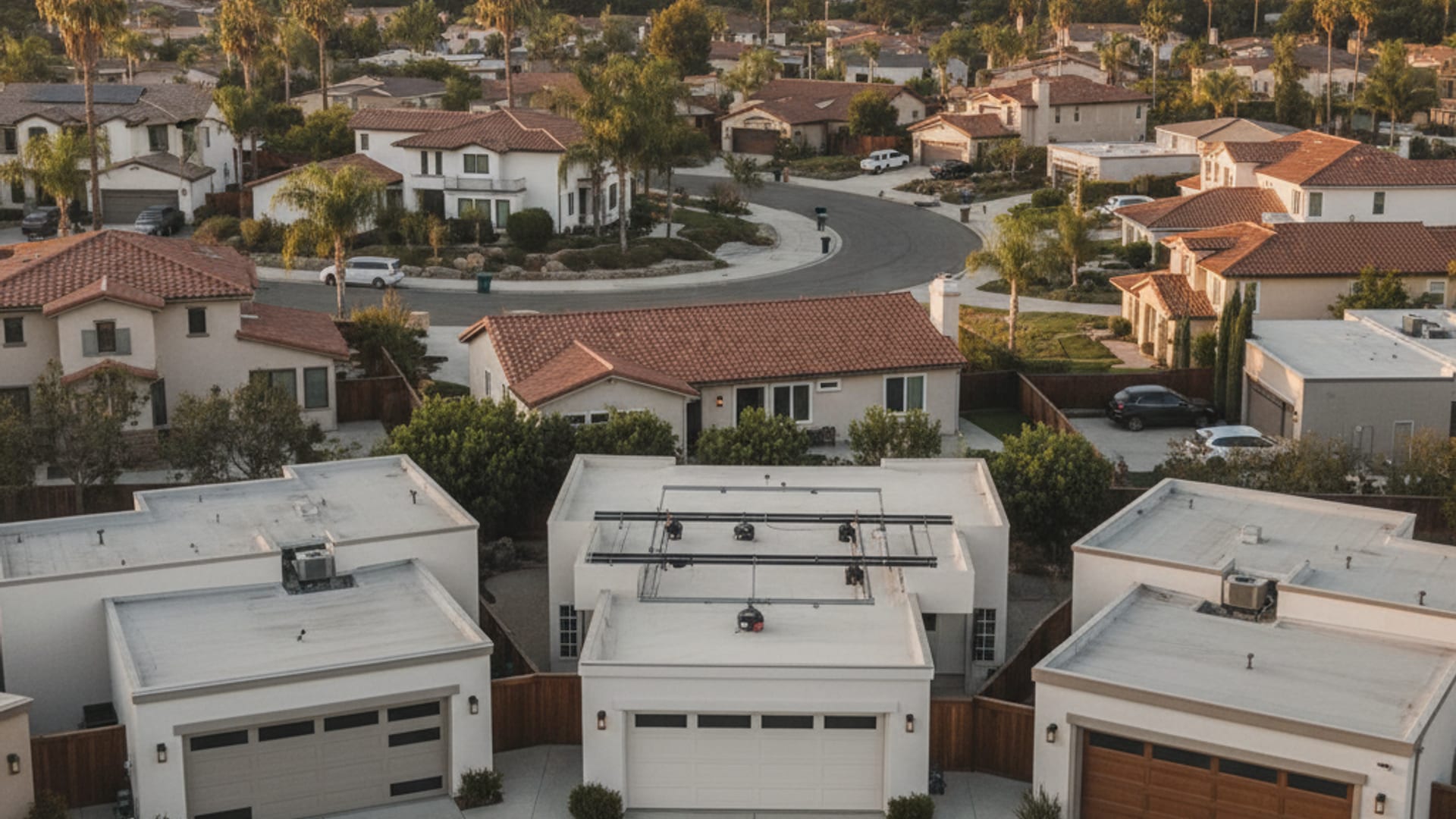 Aerial view of a San Diego County residential neighborhood with stucco homes and light-colored sectional garage doors visible along quiet streets at golden hour